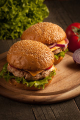 Home made hamburger with beef, onion, tomato, lettuce and cheese. Fresh burger close up on wooden rustic table with potato fries, beer and chips. Cheeseburger.