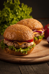 Home made hamburger with beef, onion, tomato, lettuce and cheese. Fresh burger close up on wooden rustic table with potato fries, beer and chips. Cheeseburger.