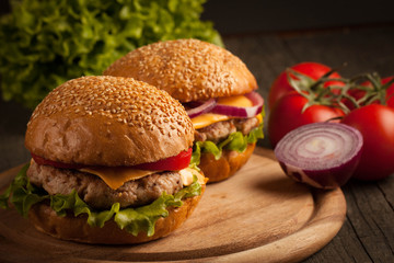 Home made hamburger with beef, onion, tomato, lettuce and cheese. Fresh burger close up on wooden rustic table with potato fries, beer and chips. Cheeseburger.