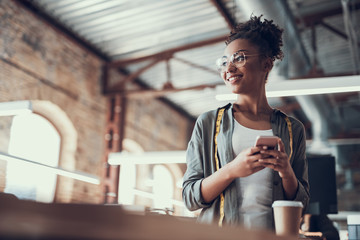 Charming afro american girl in glasses using cellphone at work