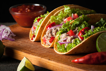 Photo of Mexican tacos with ground beef, onion, tomatoes, chili, red sauce, lettuce and lime on...