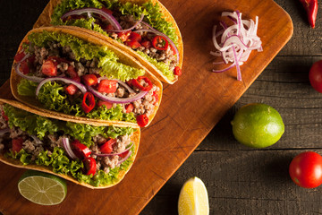 Photo of Mexican tacos with ground beef, onion, tomatoes, chili, red sauce, lettuce and lime on wooden background. Spicy and fast food concept.