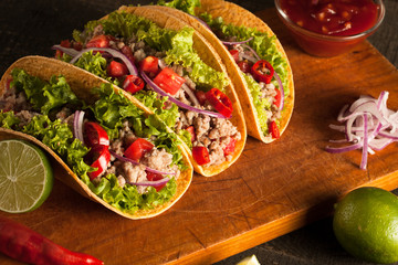 Photo of Mexican tacos with ground beef, onion, tomatoes, chili, red sauce, lettuce and lime on wooden background. Spicy and fast food concept.