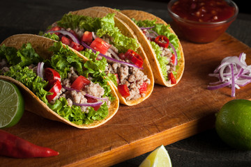 Photo of Mexican tacos with ground beef, onion, tomatoes, chili, red sauce, lettuce and lime on wooden background. Spicy and fast food concept.