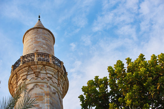 Top of the minaret of the mosque against the blue sky with a green tree