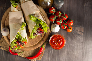 Wrap, Mexican food, fajitas, burrito, and tacos with salad, tomato, red onion and beef on wooden background. Fast food concept. 