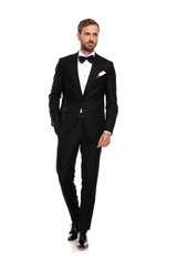 relaxed businessman in black suit looks to side while walking