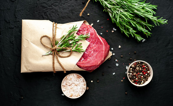 Meat From A Butcher Shop, Wrapped In Paper. A Piece Of Beef On A Concrete Black Background