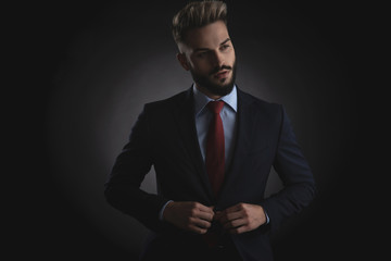 portrait of curious businessman buttoning navy suit while standing