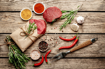 two pieces of meat from the butcher shop, one piece of meat wrapped in paper. A piece of beef in the form of a steak on a wooden background with ingredients