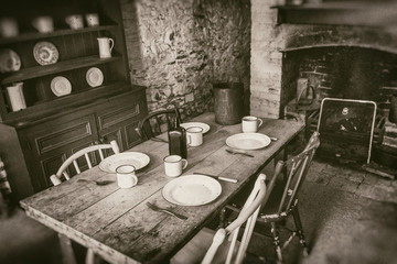 Poor peasants interior from 19th century, dining room with set wooden table and fireplace, sepia style photography - obrazy, fototapety, plakaty