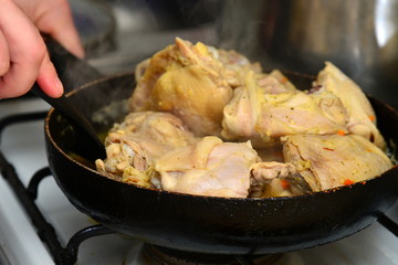 The cook mixes fried chicken in a pan with butter and spices.