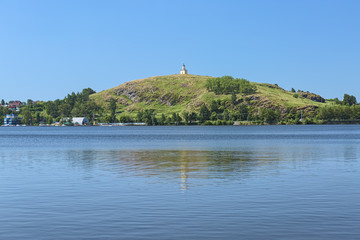 Fototapeta na wymiar Nizhny Tagil, Russia. Lisya Hill with Watchtower reflected in the water of the city pond. The Watchtower is a symbol of Nizhny Tagil. It was built in 1818 in the Classical style.