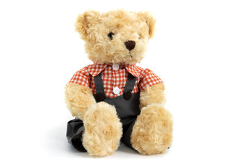 Dressed toy teddy bear in shirt and trousers is sitting on white background