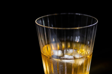 Glass of whiskey with ice on black background