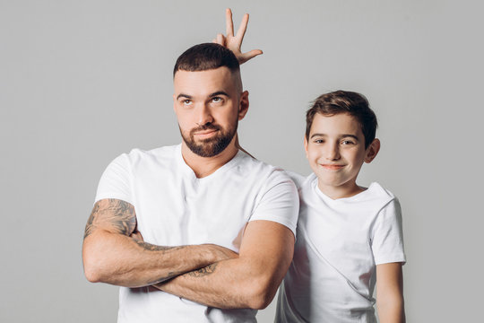 funny son holding his hands on his unhappy daddy's head close up photo. isolated grey background.kid having fun with elder brither