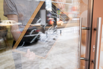 Close-up of unrecognizable man turning sign with We are open inscription on door while opening cafe