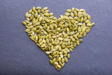 Pumpkin seeds heart overgrey stone background, top view