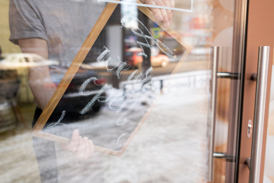 Close-up of unrecognizable man turning sign with We are open inscription on door while opening cafe