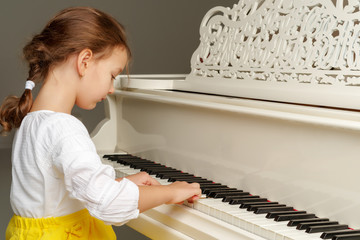 Beautiful little girl is playing on a white grand piano.