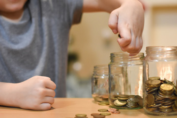Boy putting coins in a glass jar. Concept of saving. Child save money for Christmas presents