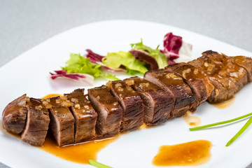 a sliced steak poured with onion decorated with lettuce leaves