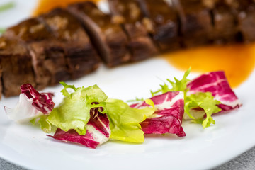 a sliced steak poured with onion decorated with lettuce leaves