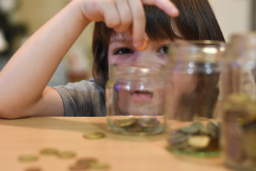 Boy putting coins in a glass jar. Concept of saving. Child save money for Christmas presents