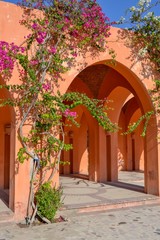 Beautiful Arabic Middle East style architecture decorated with pink flowers on the wall. Orange painting of the arches. Sidewalk. Summer season. Blue sky. Front view photography background. No people.