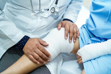 Asian senior or elderly old lady woman patient accident at arm and knee with bandage on bed in nursing hospital ward : healthy strong medical concept.  
