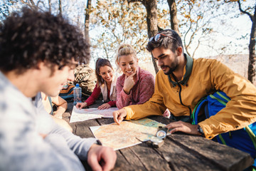 Hikers sitting on the bench at the table in the woods and looking at map. Autumn season.