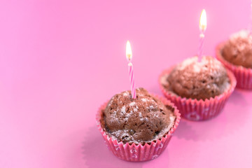 Chocolate cupcakes with candle on pink background.