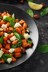 Healthy roasted sweet potato salad with spinach, feta cheese, hazelnut nuts in black plate