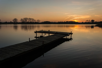 Fototapeta premium Long jetty on a calm lake and the sky during sunset.
