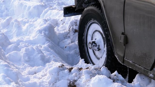 A car stuck in the snow turns the wheels. Wheel of a car turns and slips in the deep snow. Slow Motion in 180 fps. Wheels of the car stalled in the snow pit.