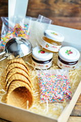 A Kit For Making Ice Cream: Spoon For Ice Cream, Ice Cream Cones, Jam, Topping, Chocolate, Sprinkles, Coconut. In Carton Wooden Natural Background. The Concept Set Surprise, Gift Idea