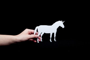 Obraz na płótnie Canvas A woman's hand holds a white unicorn with a black background paper