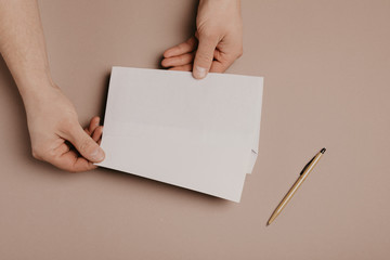 Man holds a mock-up letter or postcard in his hands with envelope on a gray background