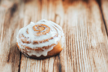 Freshly baked warm iced cinnamon buns on baked paper. Sweet homemade pastry baking on with cup of coffee and spices on wooden background.