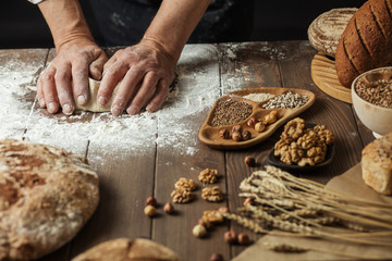 Hands of male chef cook working with dough, surrounded by bread and long loafs from whole wheat flour. Bakery concept. Homemade bakery concept