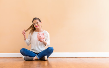 Young woman with a piggy bank against a big interior wall