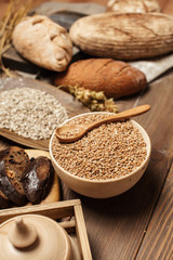 Flat Lay of different kinds of organic bread isolated on wooden table. Fresh sourdough artisan bread, loaf of rye bread with linseed and chopped pieces of buckwheat bread with nuts on chopping board.