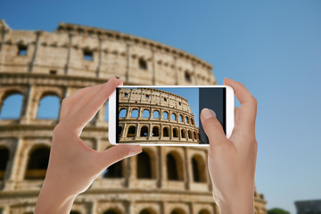 A tourist is making a photo of the Coliseum against the blue sky Rome, Italy on a mobile phone © maksim_e