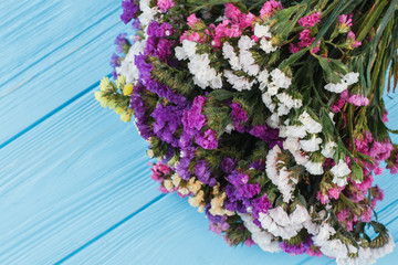 Boquet of multicolored limonium flowers close up. Blue wooden table background.