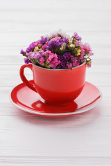 Limonium statice flowers in red coffee cup. White wood background.