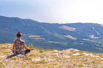 man sits on a mountain and practices yoga