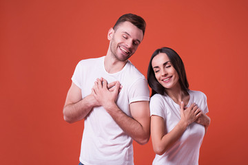 Beautiful young cute couple in love in white t-shirts holding them hands on chest. Couple in love. St Valentines day