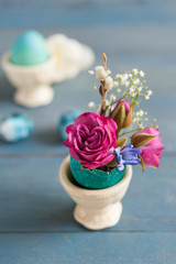 Bright Easter eggshell with flowers in stand on wooden background. Close shot