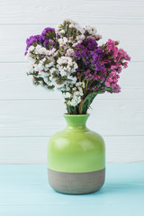 Green ceramic vase with colorful statice limonium flowers. Blue wooden background.