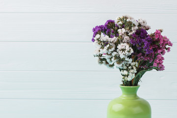 Different statice limonium flowers in a green ceramic vase. Close up. Blue wooden background.